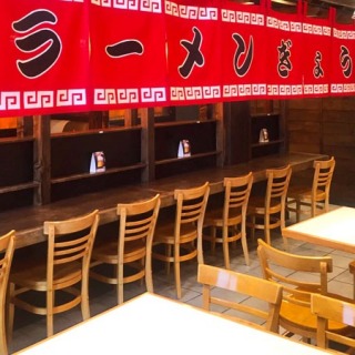 Interior of a ramen restaurant with tables and chairs arranged in front of a large banner.