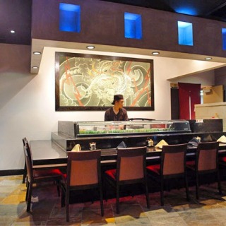 Restaurant inside with a long table and a Sushi chef at the counter.