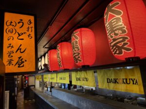 Row of red paper lanterns and yellow noren curtains above the open kitchen counter at Daikokuya Torrance.