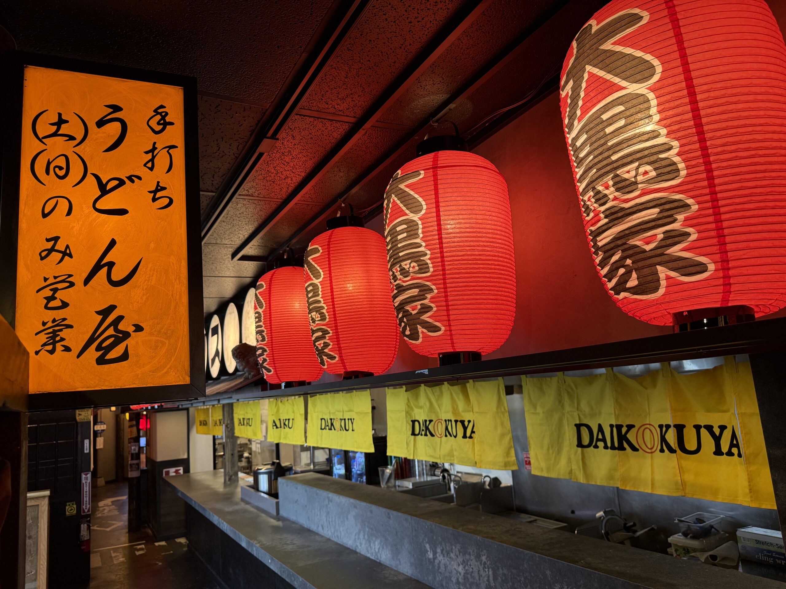Row of red paper lanterns and yellow noren curtains above the open kitchen counter at Daikokuya Torrance.